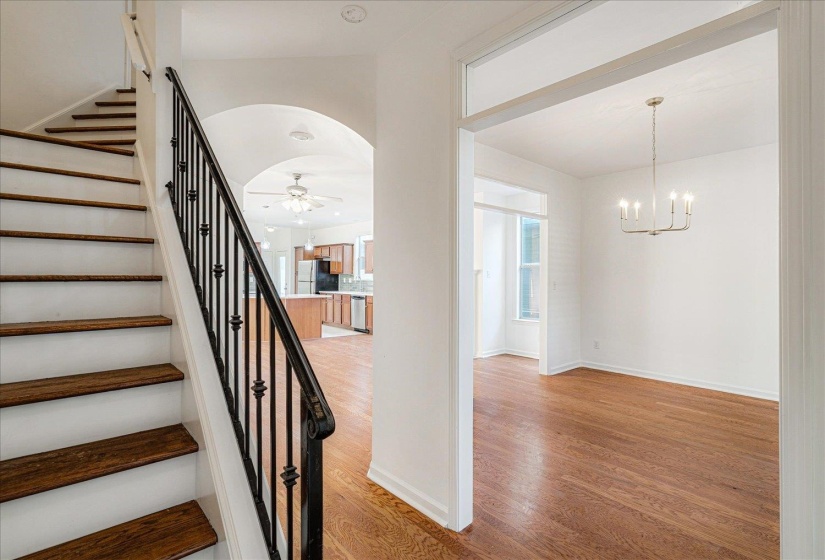 Staircase with wood finished floors, ceiling fan, a chandelier, and arched walkways