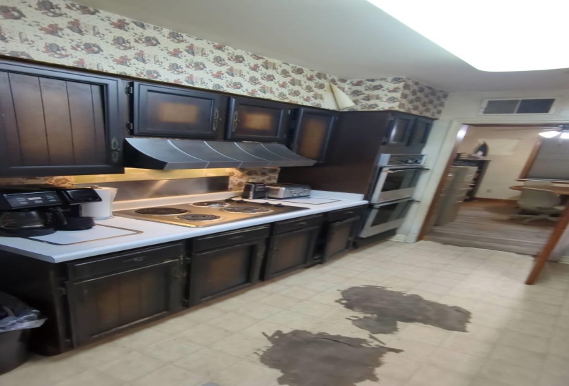 Kitchen with light countertops, wallpapered walls, light floors, stainless steel appliances, and under cabinet range hood