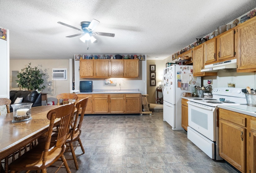 Kitchen featuring white appliances, light countertops, under cabinet range hood, a textured ceiling, and a ceiling fan