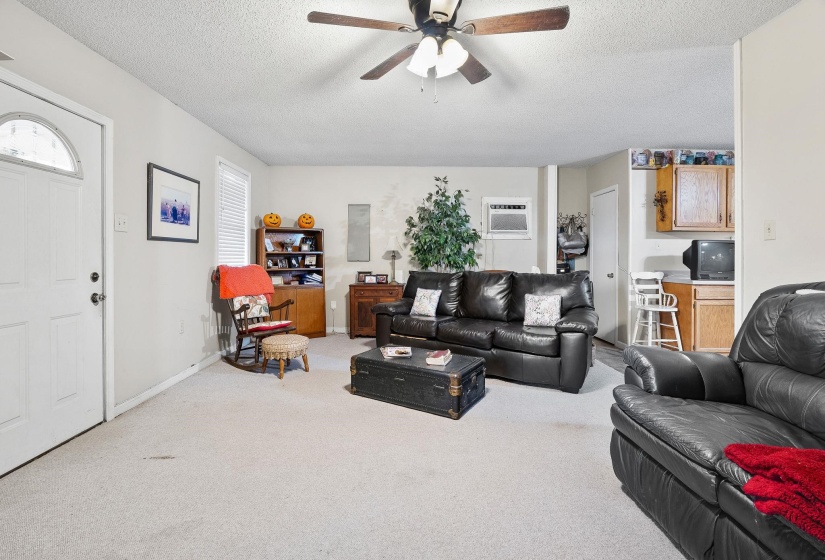 Carpeted living room featuring a textured ceiling, a ceiling fan, and an AC wall unit