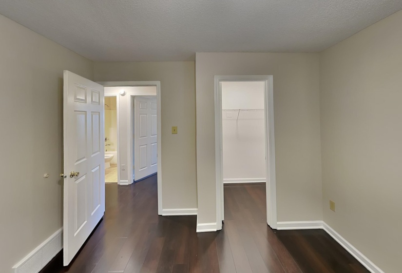 Unfurnished bedroom with a textured ceiling, a walk in closet, dark hardwood / wood-style floors, and a closet