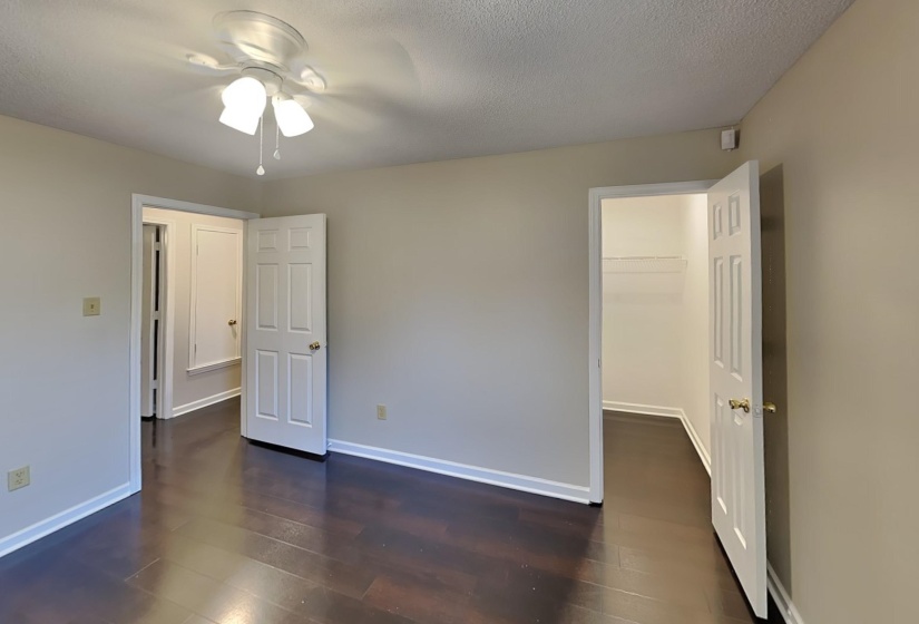 Unfurnished bedroom with ceiling fan, a textured ceiling, a spacious closet, dark hardwood / wood-style floors, and a closet