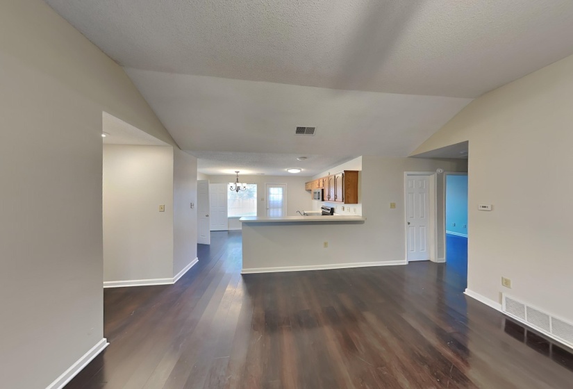 Unfurnished living room featuring dark wood-type flooring, a textured ceiling, vaulted ceiling, and an inviting chandelier