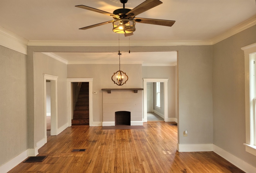 Unfurnished living room with a fireplace, wood-type flooring, crown molding, a ceiling fan, and a chandelier