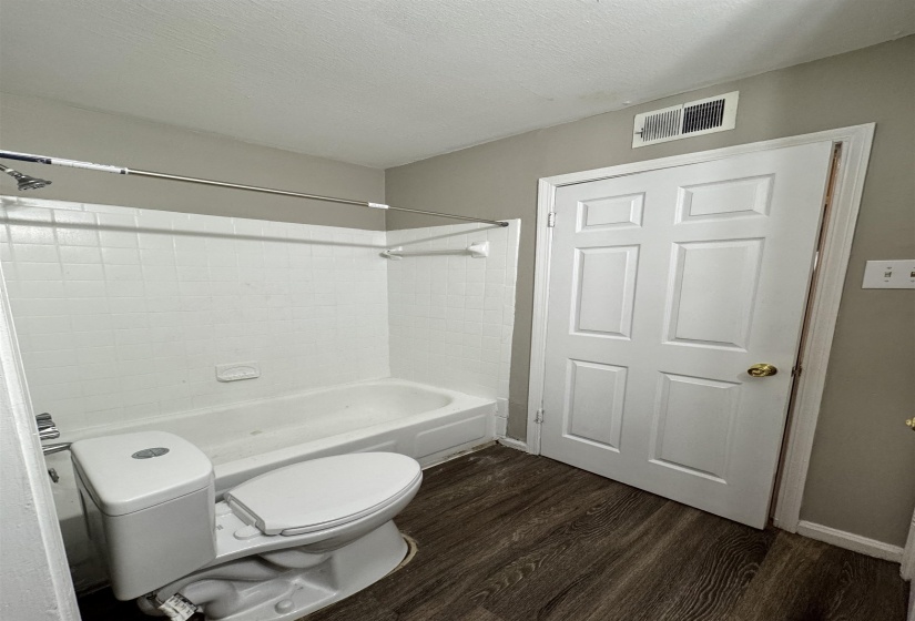 Full bathroom with dark wood-style floors, washtub / shower combination, and a textured ceiling