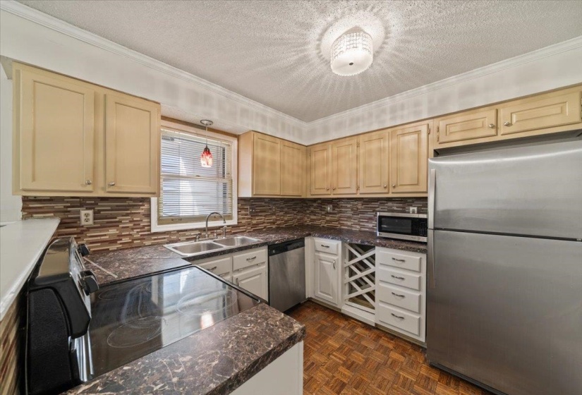 Kitchen featuring stainless steel appliances, ornamental molding, dark countertops, a textured ceiling, and pendant lighting