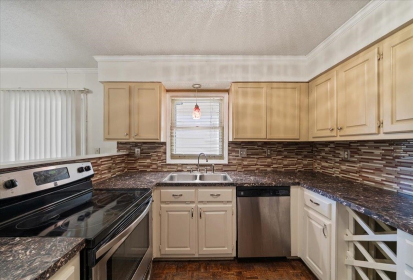 Kitchen featuring stainless steel appliances, dark countertops, a textured ceiling, decorative light fixtures, and ornamental molding