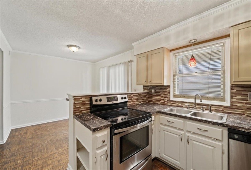 Kitchen featuring a peninsula, appliances with stainless steel finishes, dark countertops, a textured ceiling, and ornamental molding