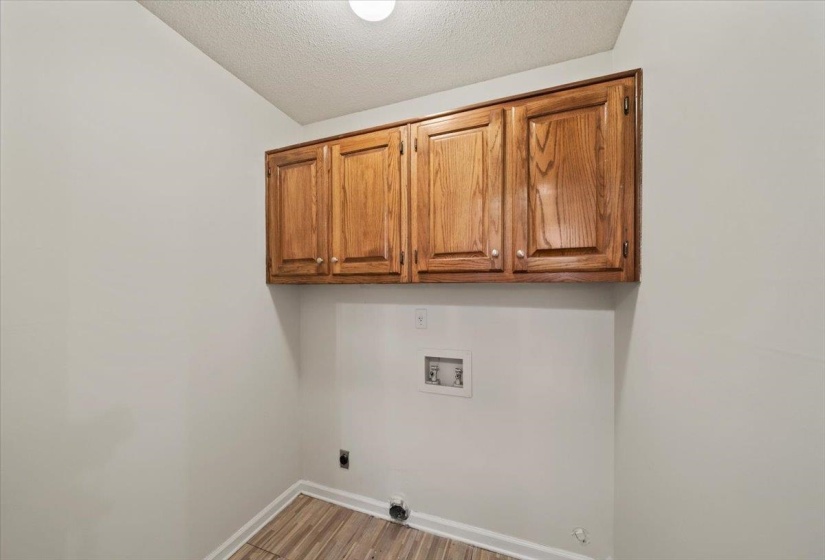 Laundry room featuring light wood-style flooring, a textured ceiling, hookup for a washing machine, cabinet space, and hookup for an electric dryer