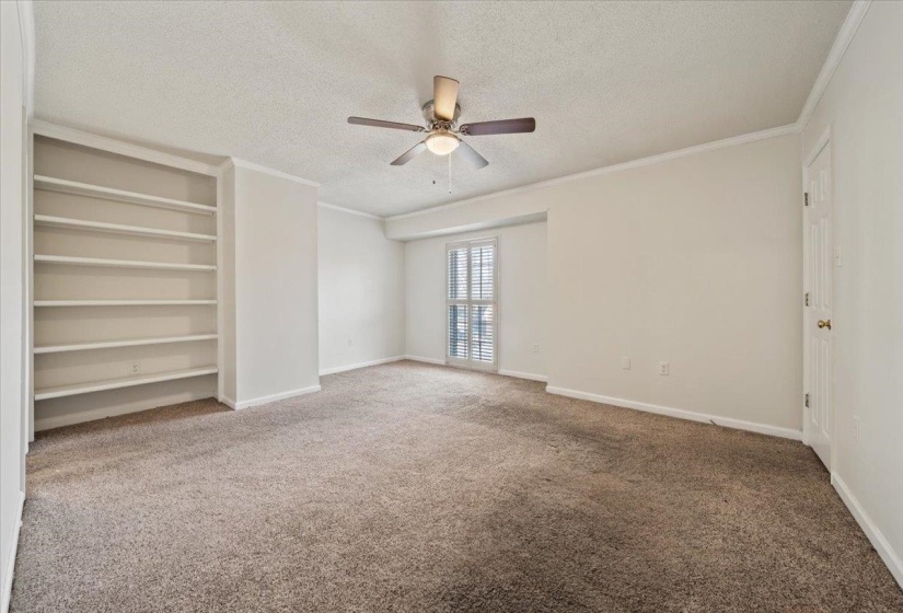 Unfurnished room with a textured ceiling, built in shelves, carpet, ornamental molding, and a ceiling fan