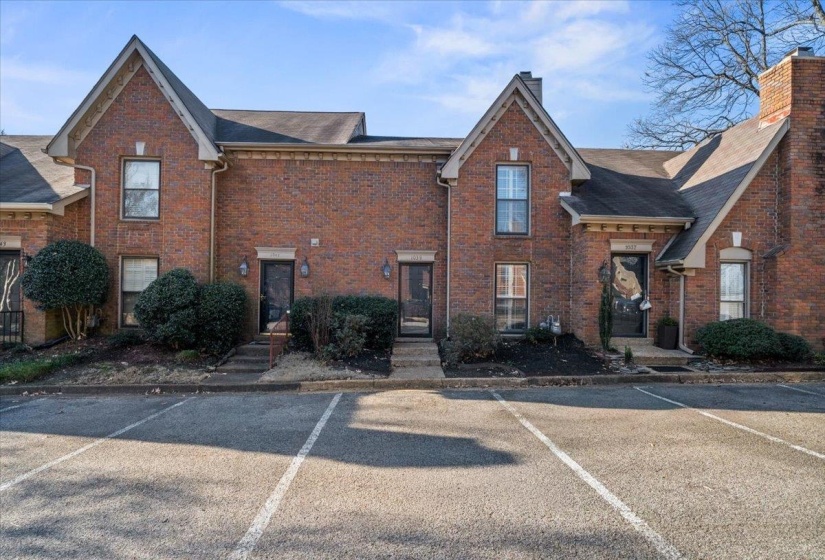 View of front facade featuring a chimney, brick siding, uncovered parking, and a shingled roof