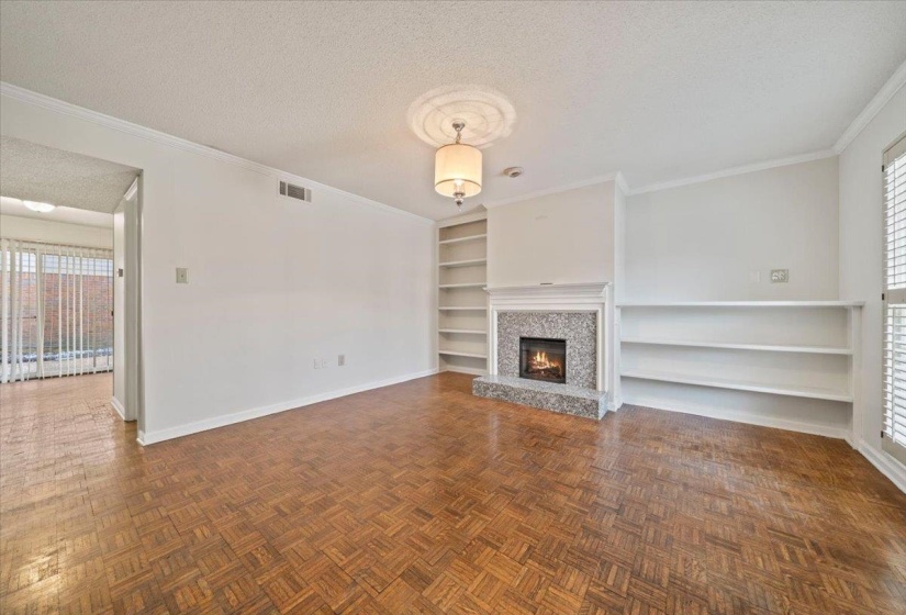 Unfurnished living room with a textured ceiling, built in shelves, ornamental molding, and a lit fireplace