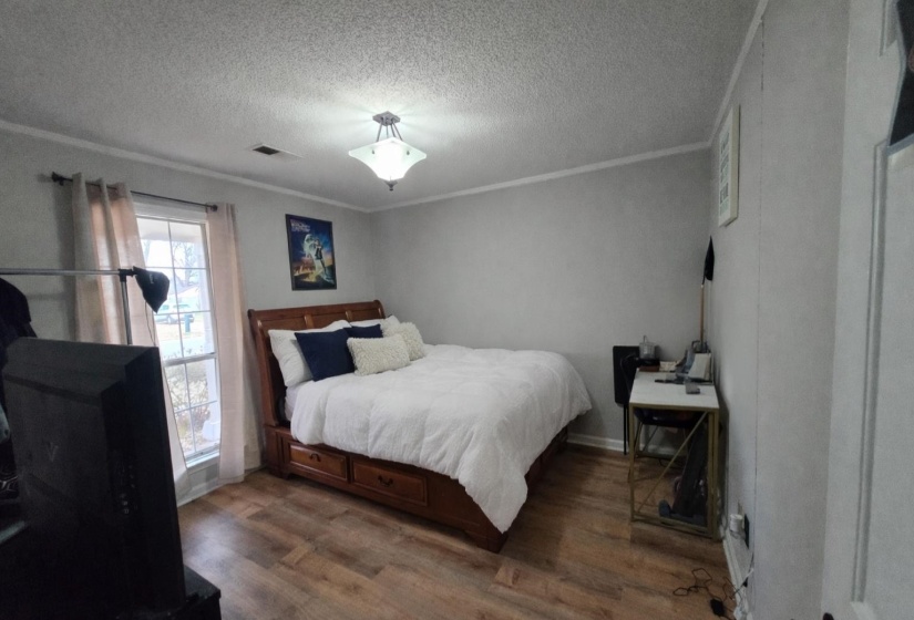 Bedroom with a textured ceiling, crown molding, and wood finished floors
