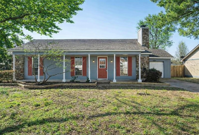 Ranch-style house featuring a porch, a chimney, a front lawn, driveway, and an attached garage