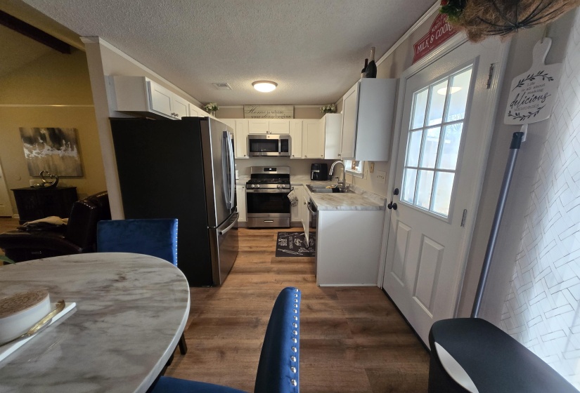 Kitchen featuring light countertops, appliances with stainless steel finishes, white cabinetry, dark wood-style flooring, and a textured ceiling