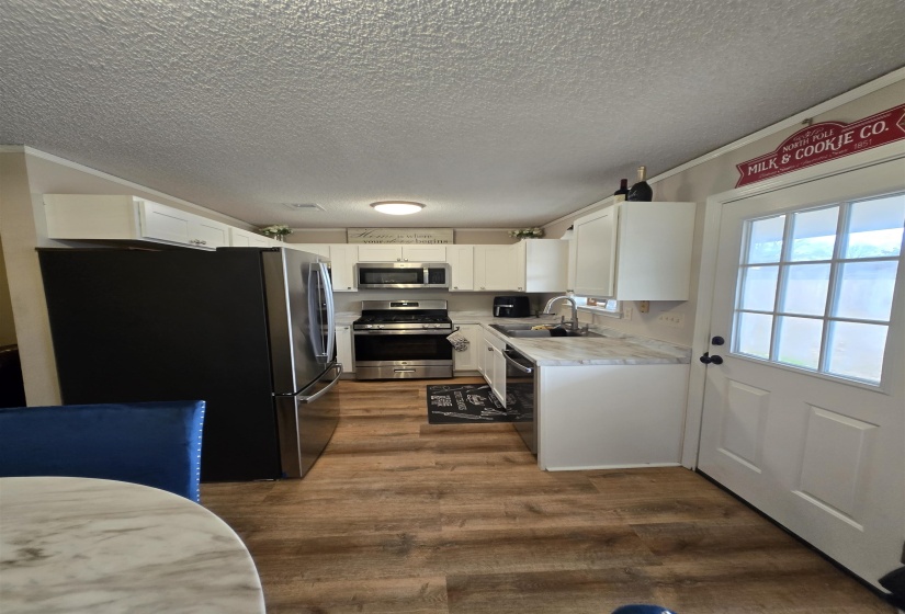 Kitchen with stainless steel appliances, light countertops, white cabinets, a textured ceiling, and dark wood-style flooring