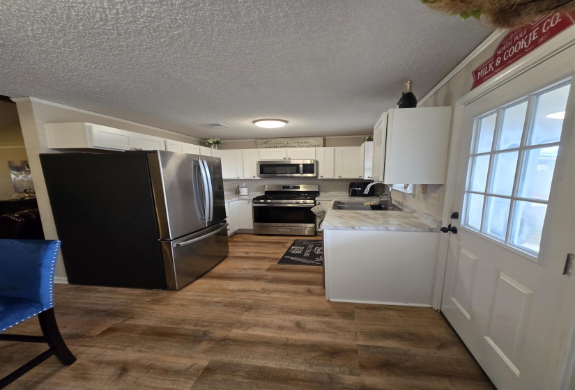 Kitchen featuring light countertops, stainless steel appliances, white cabinetry, a textured ceiling, and dark wood finished floors