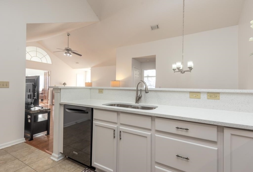 Kitchen with light stone countertops, dishwasher, white cabinets, light tile patterned floors, and vaulted ceiling