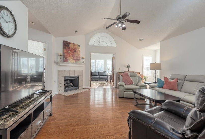 Living room featuring light wood finished floors, a tile fireplace, a ceiling fan, a textured ceiling, and high vaulted ceiling