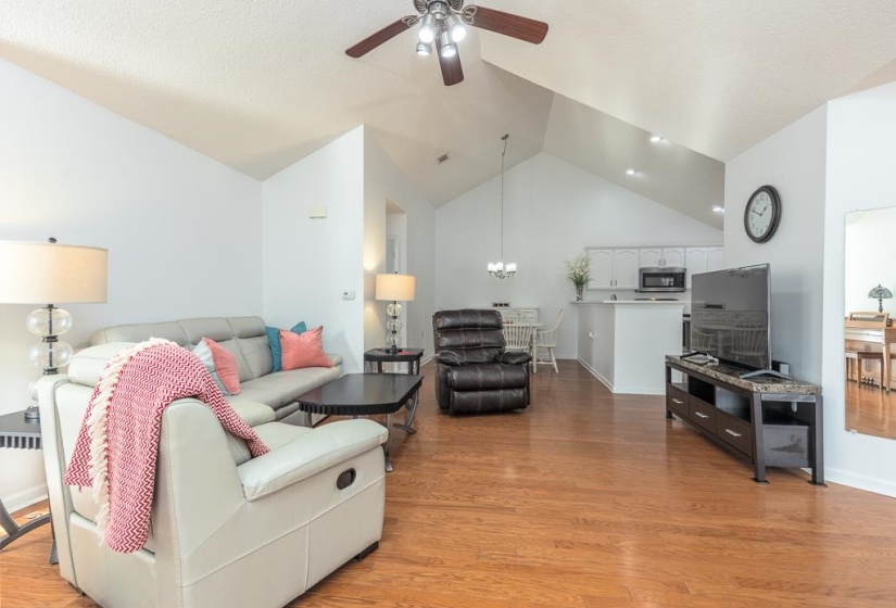 Living area featuring vaulted ceiling, light wood-type flooring, ceiling fan, and a chandelier