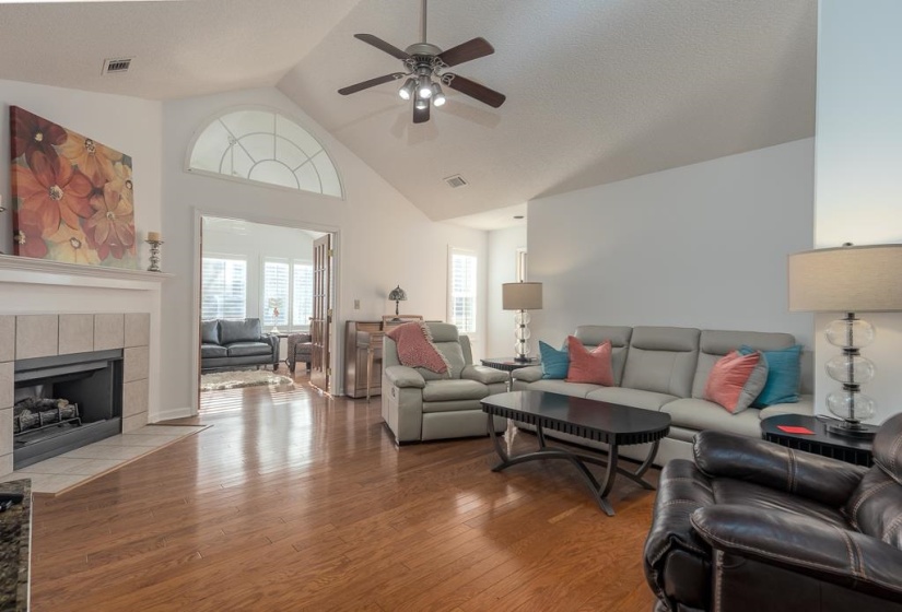 Living room featuring light wood-style floors, high vaulted ceiling, ceiling fan, a tiled fireplace, and a textured ceiling