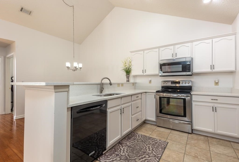 Kitchen featuring stainless steel appliances, white cabinets, a peninsula, a chandelier, and high vaulted ceiling