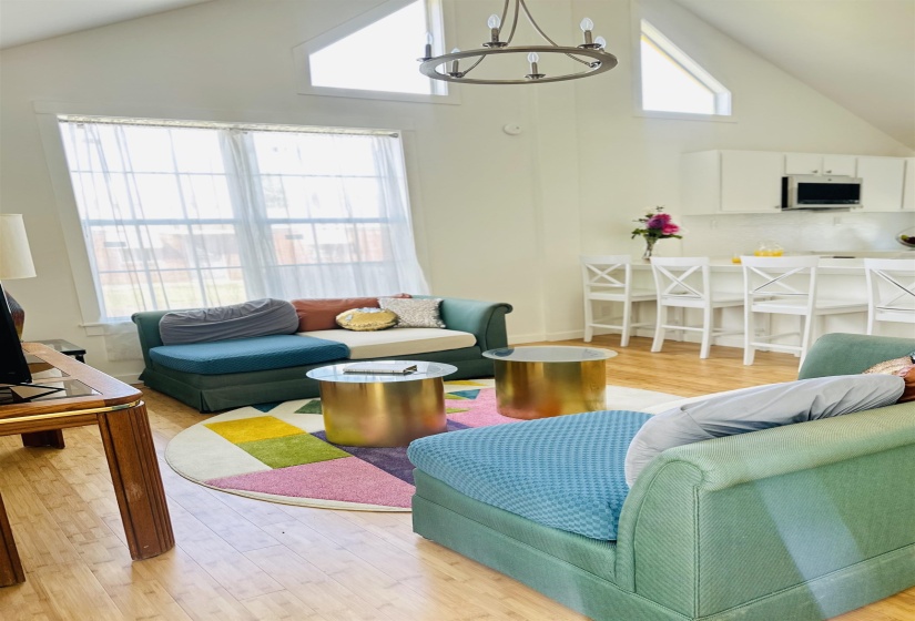 Living area with light wood-style floors, lofted ceiling, and suspended lighting