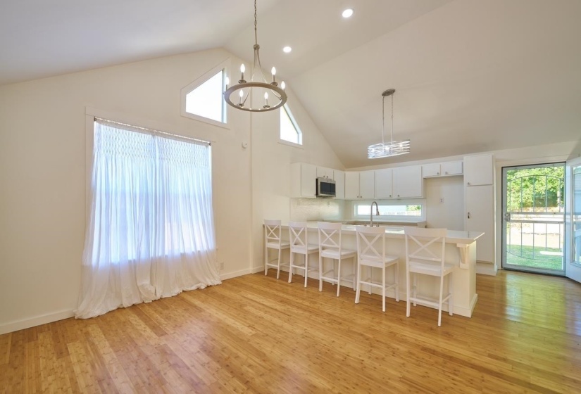 Kitchen featuring a peninsula, a kitchen bar, high vaulted ceiling, hanging light fixtures, and white cabinetry