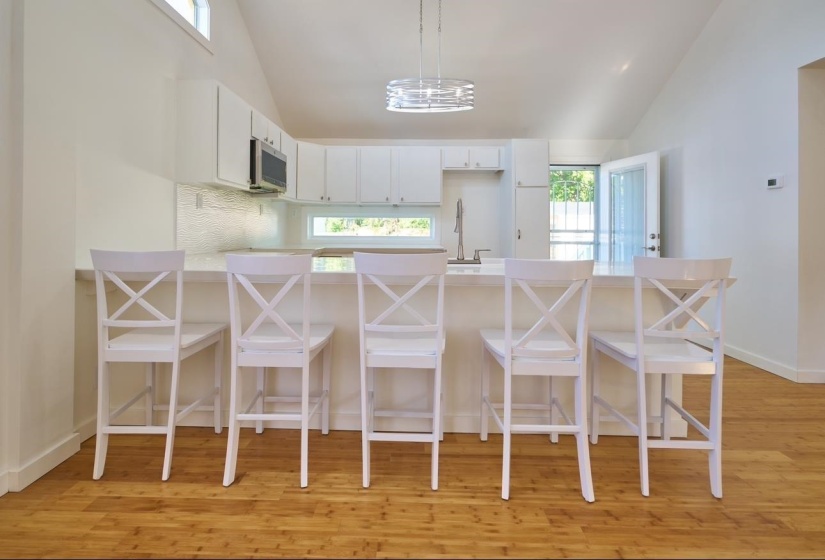Kitchen with a peninsula, white cabinets, light wood-type flooring, stainless steel microwave, and high vaulted ceiling