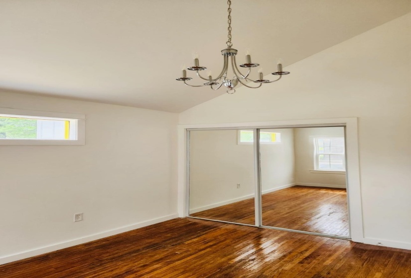 Unfurnished bedroom with hardwood / wood-style flooring, a closet, vaulted ceiling, and a chandelier
