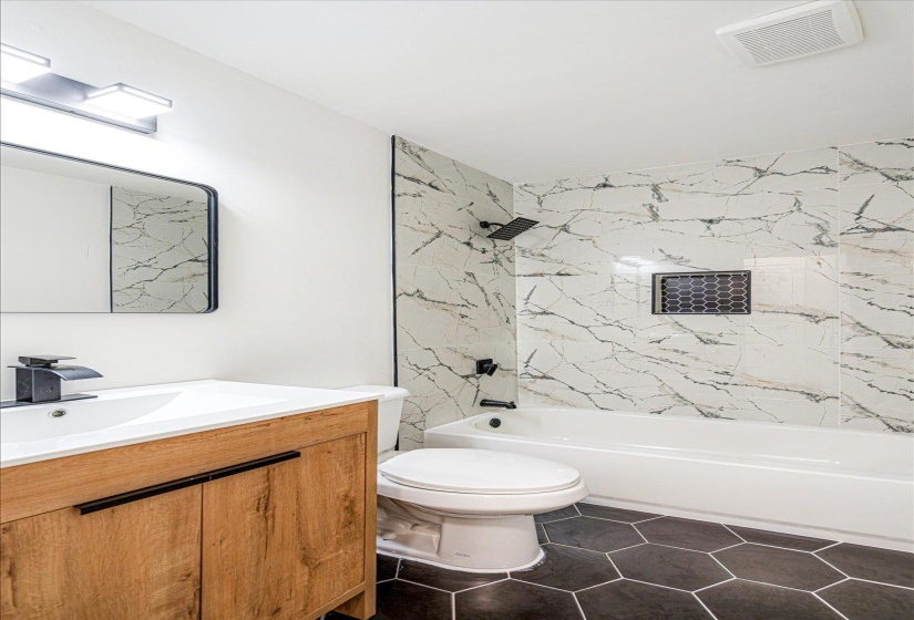Bathroom with vanity, tub / shower combination, and dark tile patterned floors