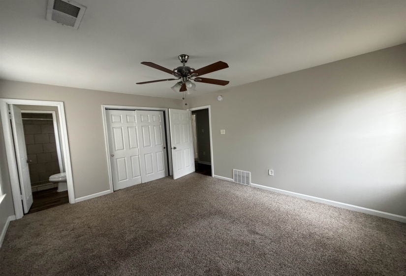 Unfurnished bedroom with a closet, ensuite bathroom, dark carpet, and a ceiling fan