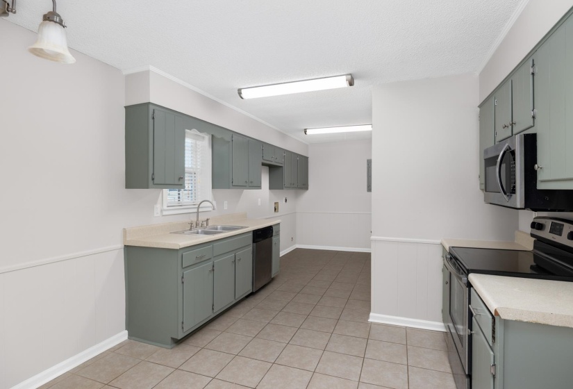 Kitchen featuring appliances with stainless steel finishes, a wainscoted wall, light countertops, light tile patterned floors, and a textured ceiling