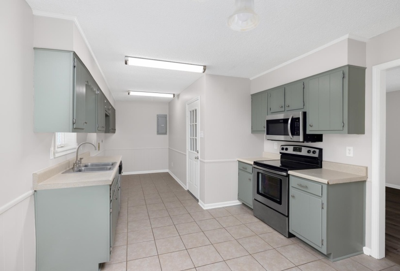 Kitchen with appliances with stainless steel finishes, light countertops, light tile patterned flooring, electric panel, and gray cabinetry