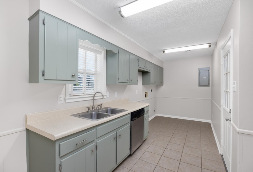 Kitchen featuring light countertops, a textured ceiling, dishwasher, light tile patterned flooring, and electric panel