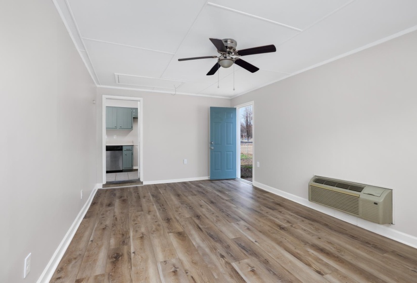 Unfurnished living room with attic access, light wood finished floors, a wall mounted AC, and ceiling fan