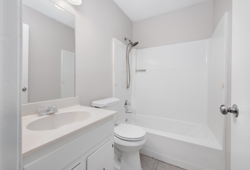 Bathroom with vanity, washtub / shower combination, light tile patterned floors, and a textured ceiling