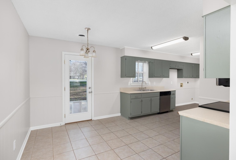 Kitchen featuring dishwasher, a chandelier, pendant lighting, a wainscoted wall, and light tile patterned flooring
