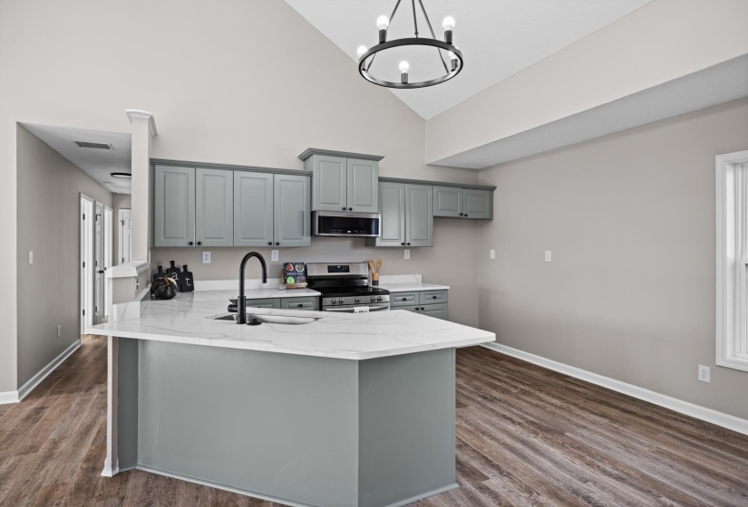 Kitchen with appliances with stainless steel finishes, gray cabinetry, a peninsula, high vaulted ceiling, and light stone countertops