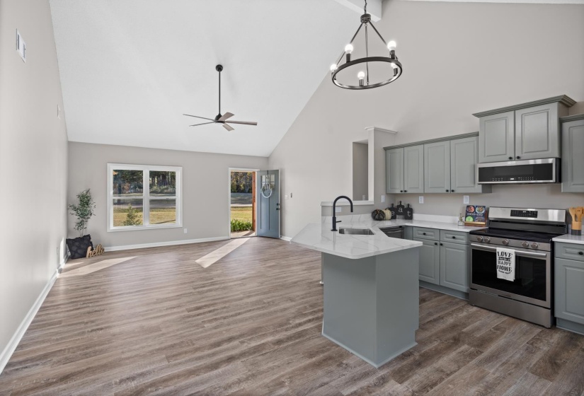 Kitchen with stainless steel electric range, gray cabinets, open floor plan, a peninsula, and high vaulted ceiling