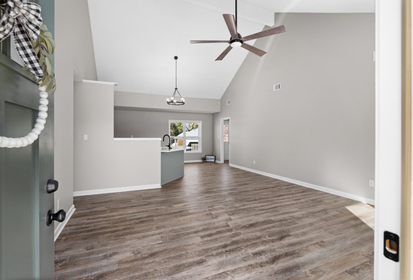 Unfurnished living room with beamed ceiling, high vaulted ceiling, dark wood-type flooring, a ceiling fan, and a chandelier