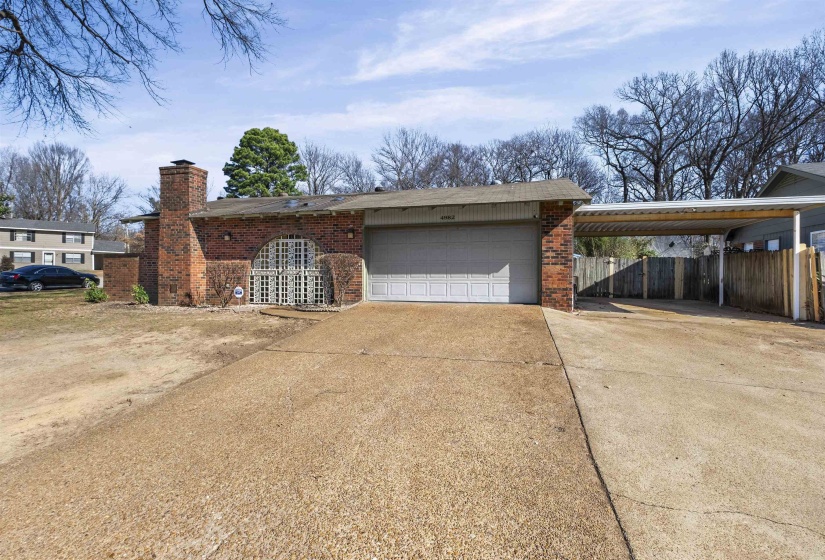View of property exterior featuring driveway, brick siding, a chimney, a carport, and an attached garage