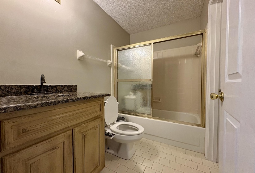 Full bath featuring a textured ceiling, vanity, light tile patterned floors, and combined bath / shower with glass door