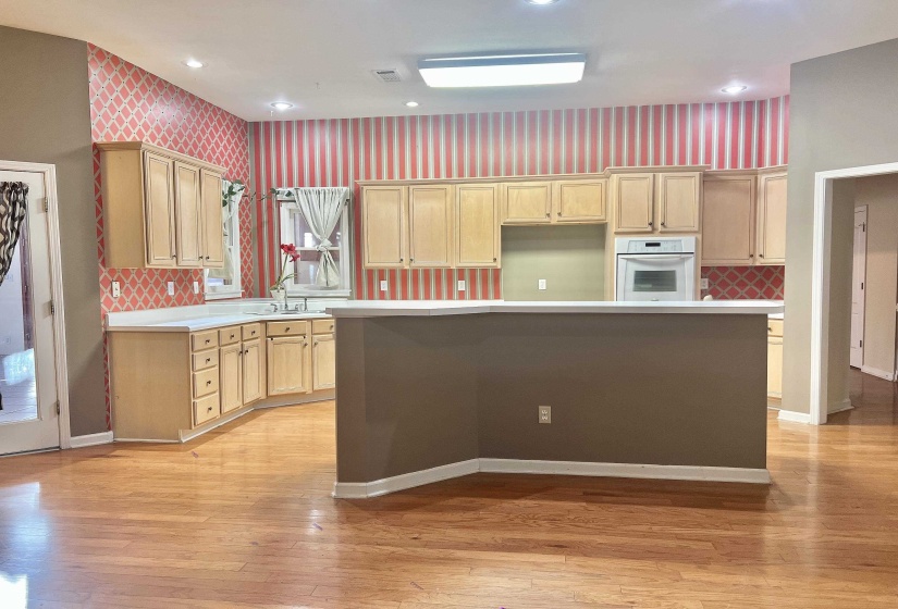 Kitchen with light brown cabinetry, light countertops, oven, a center island, and wallpapered walls