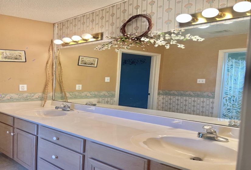 Bathroom with double vanity, wallpapered walls, and a textured ceiling