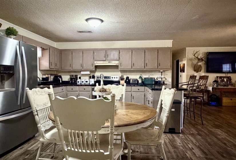 Kitchen with dark countertops, stainless steel fridge with ice dispenser, a textured ceiling, dark wood-type flooring, and under cabinet range hood