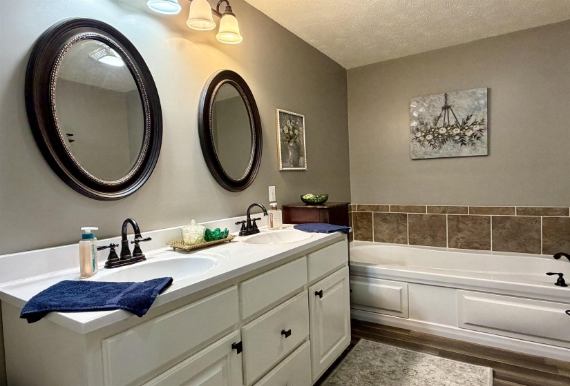 Full bathroom featuring double vanity, a garden tub, a textured ceiling, and dark wood-type flooring