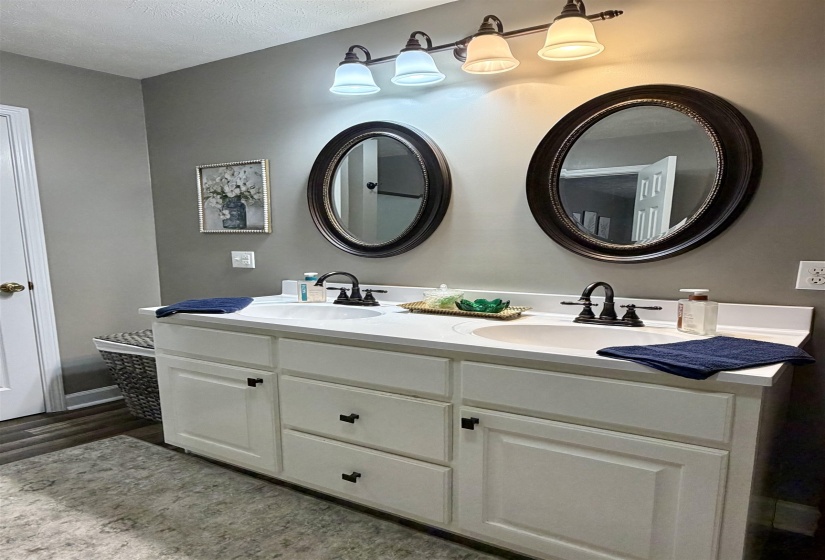 Full bath with double vanity, a textured ceiling, and light wood-type flooring