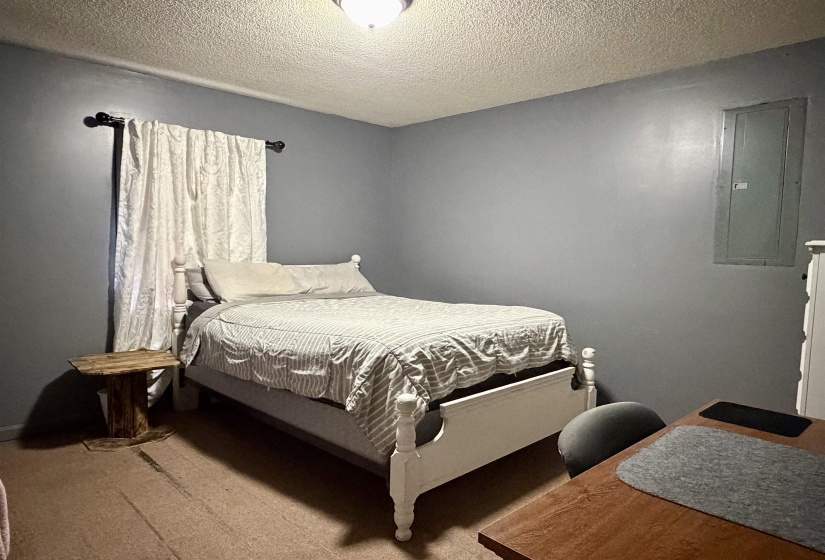 Bedroom featuring electric panel, a textured ceiling, and a desk