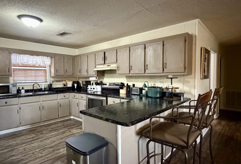 Kitchen featuring a textured ceiling, dark wood finished floors, dark countertops, appliances with stainless steel finishes, and a breakfast bar